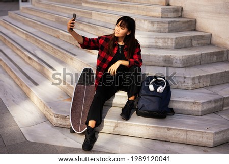 Portrait of young beautiful girl with skateboard. Happy smiling woman taking selfie photo