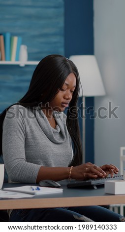 African american student sitting at desk table start typing online homework using computer browsing information on internet searching webinar courses. Black woman working remote from home