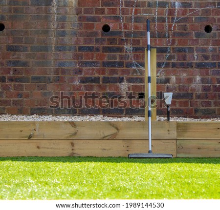 Rubber broom leaning on artificial grass in front of brick wall in a sunny urban garden Royalty-Free Stock Photo #1989144530