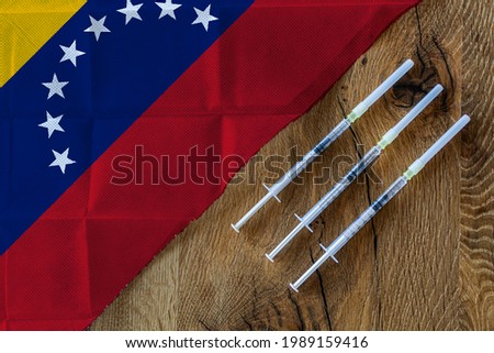 Concept of the ongoing efforts by Venezuela to deliver and distribute COVID-19 vaccines with three syringes on a wooden table ready to use with a Venezuelan Flag. Copy Space for Text and Graphics.