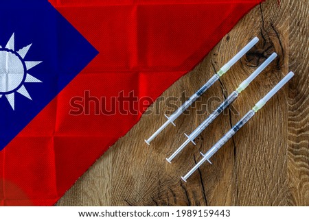 Concept of the ongoing efforts by Taiwan to deliver and distribute COVID-19 vaccines with three syringes on a wooden table ready to use with a Taiwanese Flag. Copy Space for Text and Graphics.