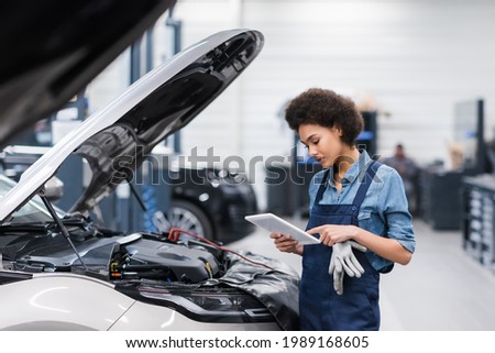 young african american mechanic holding digital tablet near car with open hood in auto repair service Royalty-Free Stock Photo #1989168605