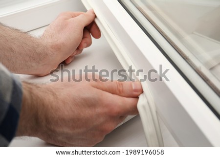 Worker putting rubber draught strip onto window indoors, closeup Royalty-Free Stock Photo #1989196058