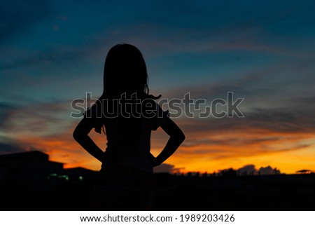 Silhouettes of a child standing she looking at the sky at sunset, Sky blue and orange light of the sunset