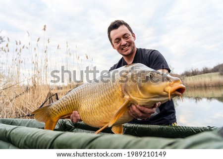 Fisherman holding a huge carp at the lake. 