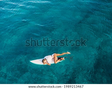 Attractive surf girl relaxing on surfboard in transparent ocean. Aerial view with surfer woman