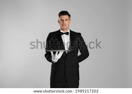 Handsome butler with tray on light grey background