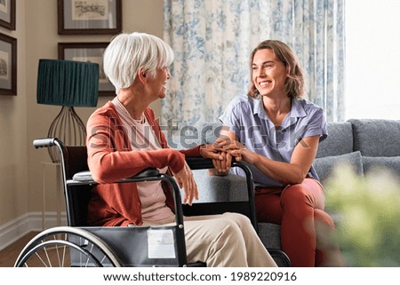 Mature woman comforting senior mom sitting on wheelchair at nursing home. Cheerful woman talking to old disabled mother at elder care centre. Loving caregiver taking care of elderly woman at home. Royalty-Free Stock Photo #1989220916