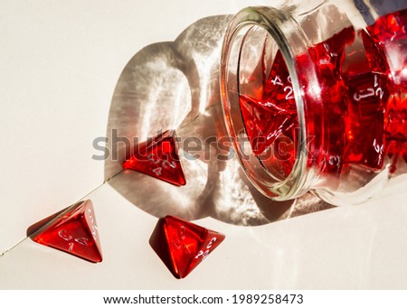 Close-up image of red 4-sided dice spilling out of a glass bottle onto a notebook. The sunlight shining through the bottle creates a beautiful heart shape shadow
