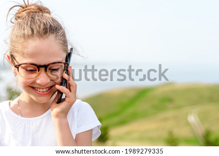 Portrait of a little girl with glasses talking on the phone on a summer day