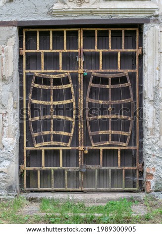 Old doorway with a rusty metal barred door in the shape of wine barrels. Padlocked and abandoned.
