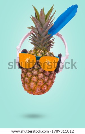 Creative trendy summer invitation card with pineapple wearing sunglasses made of fresh orange and headphones on pastel blue background. Minimal scene of fun, party, trend and funny art design.