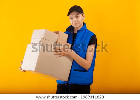 Pretty blonde girl with ponytail in black outfit and blue vest posing with large mockup box. High quality photo for retail, business, delivery and advertising.