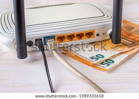 Two fifty 50 euro bill banknotes and white Wi-Fi wireless router with connected cables on a white wooden desk. Concepts of earn money online, e-commerce, online shopping and bill payments. Close-up. Royalty-Free Stock Photo #1989331658
