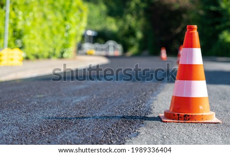 Construction cones marking part of road with a layer of fresh asphalt.  Royalty-Free Stock Photo #1989336404
