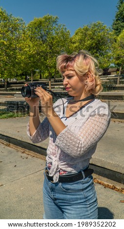 short haired girl with a reflex camera in her hands, young woman taking pictures in the park with her reflex camera, short curly hair photographer and white blouse in the park