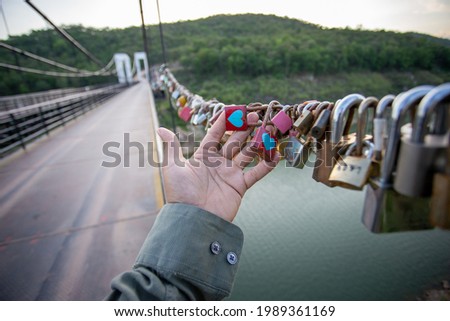 selective focus padlock on suspension bridge The padlock has two blue heart-shaped stickers. in the hand of a man, The same color indicates that gender is not separated. It is a symbol of eternal love