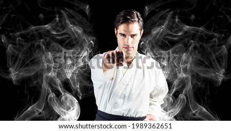 Composition of male martial artist over trails of smoke on black background. sport and competition concept digitally generated image.