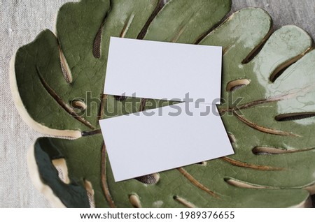 Summer stationery still life. Blank business card mockup on ceramic plate of monstera sheet. Gray linen tablecloth fabric background. Branding concept. Mediterranean design. Styled flat lay