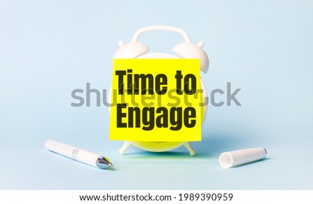 On a light blue background - a white handle and an alarm clock with a bright yellow sticker glued to it with the text TIME TO ENGAGE