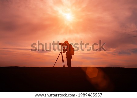 silhouette of Travel photographer standing with a camera mounted on a tripod
