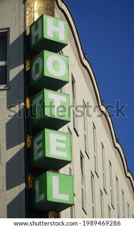 Vertical Hotel signboard over the entrance to the building. Vertical green hotel sign mounted on beige facade of hotel. White letters on green cubes.