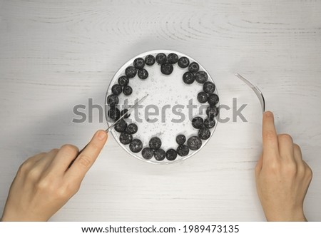 hands with a knife and fork next to a white little blueberry cake. High quality photo