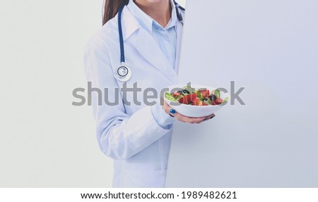 Portrait of a beautiful woman doctor holding a plate with fresh vegetables standing near blank. Woman doctors