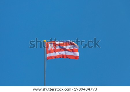 The flag of Alkmaar on the pole waving on the air with blue clear sky as background, The flag consists of three white and three red stripes and includes the city’s castle. 