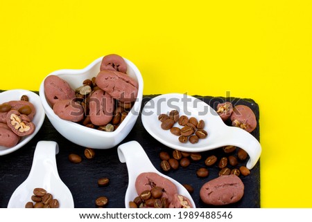Pickan nuts and coffee beans, yellow background. Macro concept. As an element of packaging design, white and black dishes