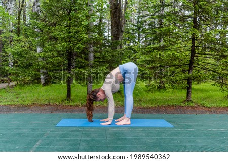 Candid red-haired woman doing yoga outdoors in the park. Sportswear and yoga mat. Wellness and sports lifestyle concept. Copy space
