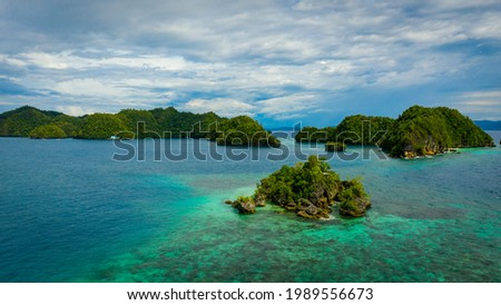 Panoramic picture in soccoro, philippines, with a rocky islet surrounded by turquoise water located in the foreground, impresive green hills and a cloudy sky in the background