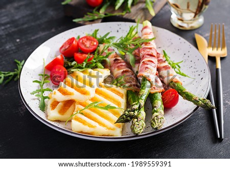 Grilled halloumi cheese salad with tomatoes and asparagus in strips of bacon on plate on dark background. Healthy  food.