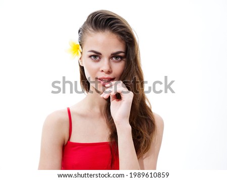 pretty brunette woman in a red t-shirt with a yellow flower in her hair touches her face with her hand