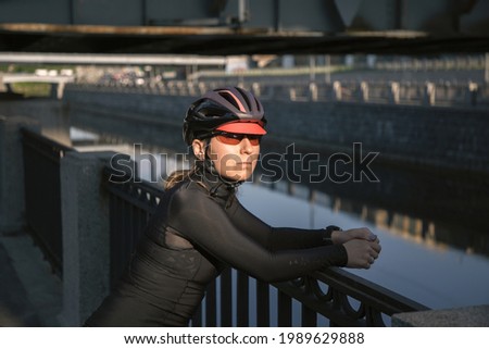 Portrait of a female cyclist wearing a helmet and goggles, lit by the sun during a morning workout on the waterfront in the city.