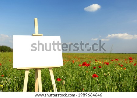 Wooden easel with blank canvas in poppy field on sunny day