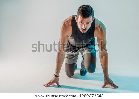 Young bearded concentrated european runner on start. Sportsman wear sports uniform and looking at camera. Isolated on turquoise background. Studio shoot. Copy space Royalty-Free Stock Photo #1989672548