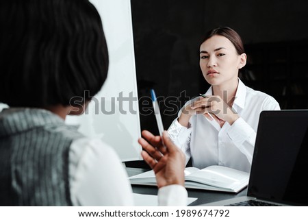 Serious young asian office worker interviewing african american woman while sitting at table with documents