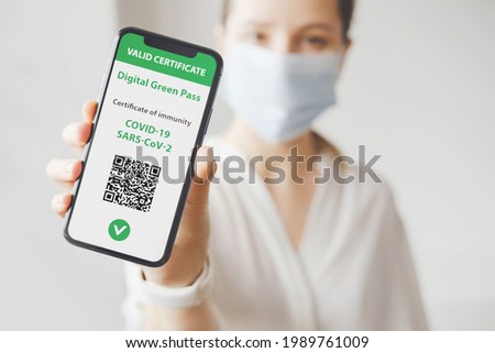 Young caucasian woman in mask holding smartphone with digital green pass and QR code on the screen. Health passport or certificate of immunity. Traveling without restrictions. Vaccinated person Royalty-Free Stock Photo #1989761009
