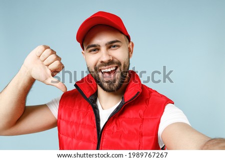 Close up professional delivery guy employee man in red cap white T-shirt uniform workwear work as dealer courier doing selfie isolated on pastel blue color background studio portrait. Service concept
