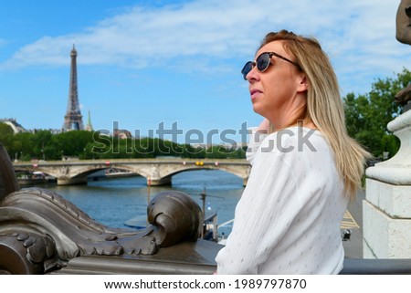 Portrait of a pretty blonde woman in town by the water, standing on a beautiful historic bridge. City and river in the background blurred deliberately.