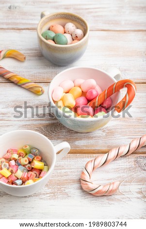 Heap of multicolored caramel candies in cups on white wooden background. side view, close up.