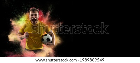 The professional football, soccer player and human emotions concept. The win, winner, victory concepts. Forward. One sportsman in explosion of colored neon powder isolated on dark background