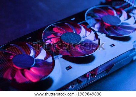 A graphics card with a row of fans with a cyanotic purple backlight in a futuristic design. Powerful gaming graphics card for video games and cryptocurrency mining. Dark key, top view Royalty-Free Stock Photo #1989849800