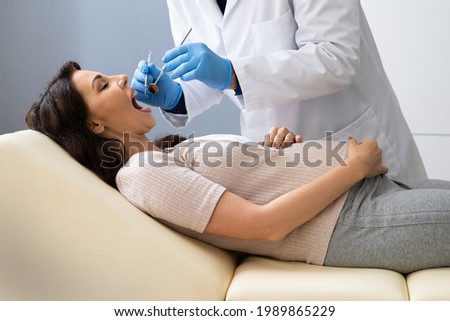 Dentist Treating Teeth Of Young Pregnant Woman Patient Lying In Clinic Royalty-Free Stock Photo #1989865229