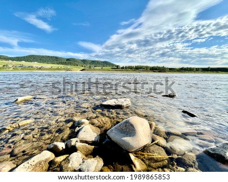 Rocky river bank with clear clear water. View of the other bank across the river, against a blue sky with clouds. Close-up shot of a rocky beach.