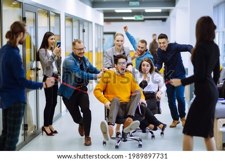 Young colleagues group having fun together, riding on chairs in office, diverse excited office workers enjoying break, laughing, engaged funny activity, celebrating corporate success. Royalty-Free Stock Photo #1989897731