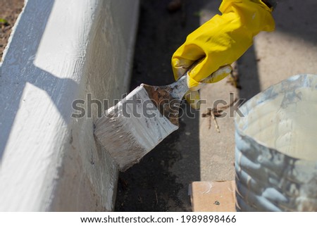 Painting borders with white paint. Applying oil paint to asphalt. Creation of markings for pedestrians. Paint brush. Work as a painter. Painting the surface with a thick layer of paint.