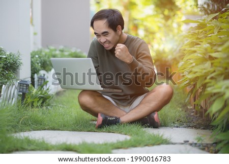 Young man sitting on the grass with laptop feeling happy ,Smiling young man showing signs of success in good work The idea of running a successful business of the company.