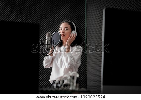 Asian female singer with a passion for music and microphone. While playing her guitar in a professional studio. Music concept, sound recording concept. Royalty-Free Stock Photo #1990023524